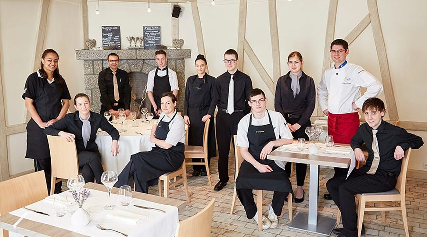 Une douzaine de membres du personnel d'un restaurant, en tenues noires et veste de chef, posent autour de tables dressées devant une cheminée en pierre.